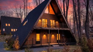 A triangular wooden cabin with a balcony, surrounded by trees. - A-Frame Escape | Firepit Nights + Lake Days (Coolbaugh Township)