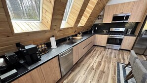 A modern kitchen with wooden cabinets, a black countertop, and a large window. - A-Frame Escape | Firepit Nights + Lake Days (Coolbaugh Township)