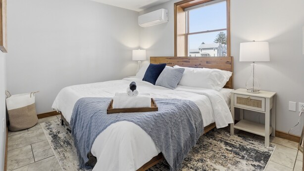 Un dormitorio con cama, lámparas de noche, una ventana, una mesita de noche y un aire acondicionado de pared.