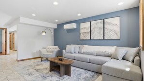 Una sala moderna con un sofá gris, una mesa de centro de madera y una lámpara de pie.
