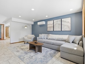 Una sala moderna con un sofá gris, una mesa de centro de madera y una lámpara de pie.