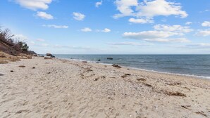En strand med sten og klipper, en klar himmel og et roligt hav.