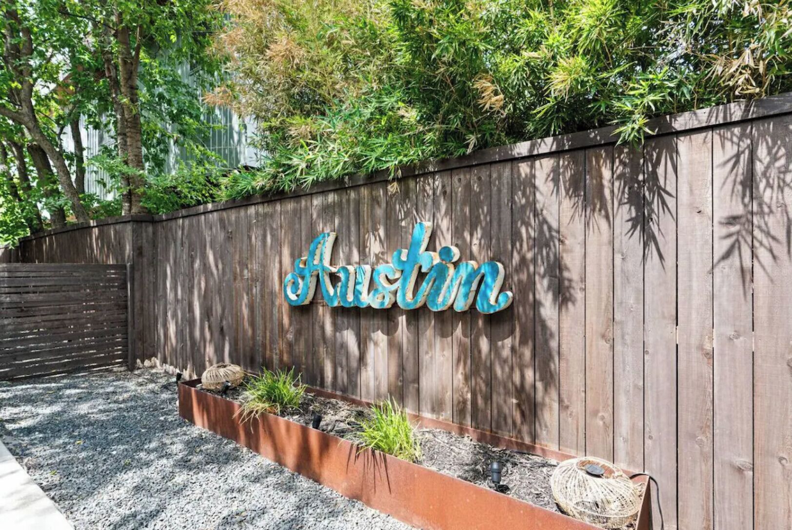 A wooden wall with the name 'Austin' in decorative letters, a garden bed with plants, and a woven basket.