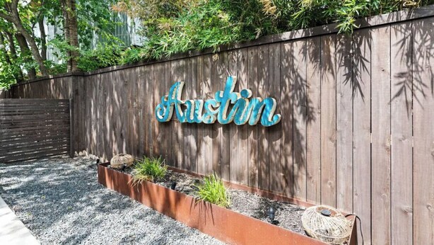Pared de madera con el nombre 'Austin' en letras decorativas, una jardinera con plantas y una cesta tejida.