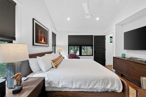 A modern bedroom with a large bed, a flat-screen TV, a ceiling fan, and a window with a view of greenery. - Zilker Modern + Cowboy Pool - Haven! (Austin)