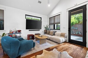 A modern living room with a flat-screen TV, a blue sofa, a wooden coffee table, and a beige sofa. - Zilker Modern + Cowboy Pool - Haven! (Austin)