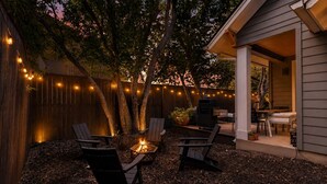 Un patio al aire libre con una fogata, zona de estar y luces colgantes.