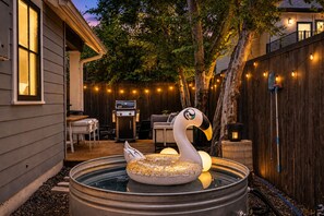 Un pati amb una banyera d'hidromassatge, un flotador amb forma de cigne, una barbacoa i llums penjades.