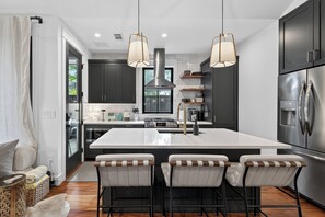 A modern kitchen with a central island, bar stools, stainless steel appliances, and pendant lighting. - Zilker Modern + Cowboy Pool - Haven! (Austin)