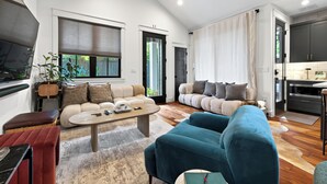 Amplia sala de estar con un sofá, una mesa de centro y un televisor. Zona de cocina con armarios y un refrigerador.
