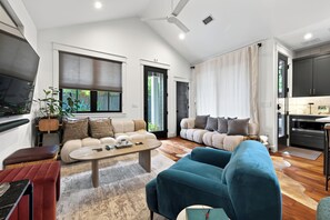A spacious living area with a sofa, a coffee table, and a TV. There is a kitchen area with cabinets and a refrigerator. - Zilker Modern + Cowboy Pool - Haven! (Austin)