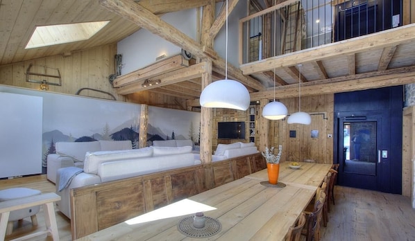 Ein rustikales Interieur mit Holzbalkendecke, einer Sofagarnitur, Pendelleuchten und einem Esstisch.