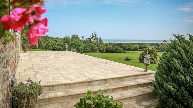 Una escalera de piedra que lleva a una terraza con vistas al mar y al verdor.