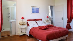 Un dormitorio con una cama, dos mesitas de noche, una mesilla auxiliar, un cuadro enmarcado en la pared y una puerta.