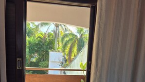 Janela com vista para uma piscina, deck de madeira e vegetação.