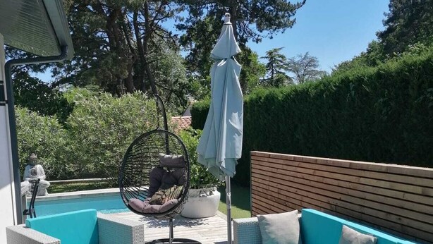 Um pátio externo com móveis de vime, uma cadeira suspensa e uma piscina.