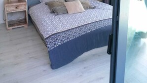 Quarto com cama, mesa de cabeceira, obra de arte na parede e porta de correr de vidro.