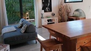 Um espaço de estar moderno com sofá, mesa de jantar de madeira e vista para o verde lá fora.