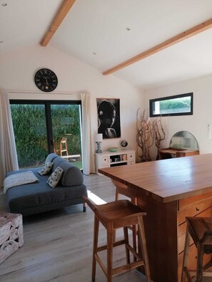 A modern living space with a sofa, wooden dining table, and a view of greenery outside. - NEW HOUSE +BUNGALOW+HEATED POOL&JACUZI (Angresse)