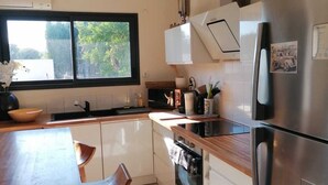 Cozinha moderna com mesa de madeira, duas cadeiras, forno embutido e geladeira de aço inoxidável.