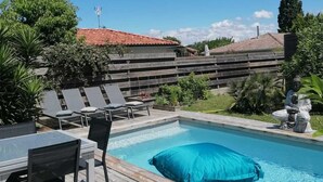 Piscina com deck de madeira, cadeiras de descanso e mesa.