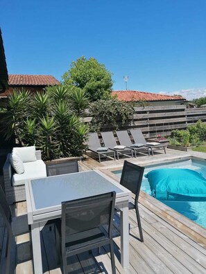 Un espace aménagé au bord de la piscine, comprenant une table et des chaises, des fauteuils de relaxation et une piscine.