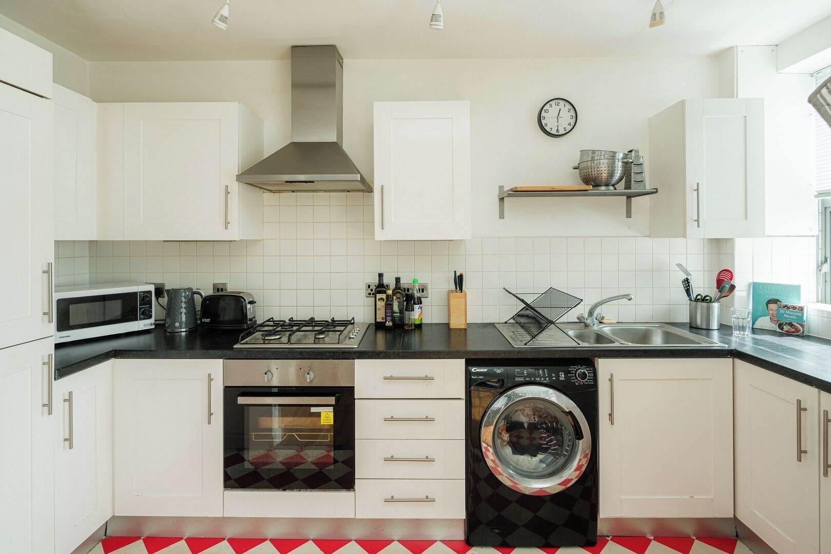 A modern kitchen with white cabinets, a microwave, a gas stove, a dishwasher, and a red and white checkered floor.