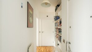 A hallway with a wooden floor, white walls, a white door, and a bookshelf filled with books. - Bright Spacious 1BR Flat in Vibrant Dalston (London)