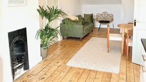 Amplia sala de estar con piso de madera, un sofá verde, una mesa de comedor y una araña.
