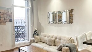 A living room with a sofa, a coffee table, a decorative mirror, and a view of buildings through a window. - Stunning apartment in Marseille with WiFi (Marseille)