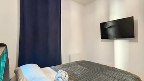 A bedroom with a bed, a dark curtain, a flat-screen TV mounted on the wall, and a textured blanket. - Stunning apartment in Marseille with WiFi (Marseille)