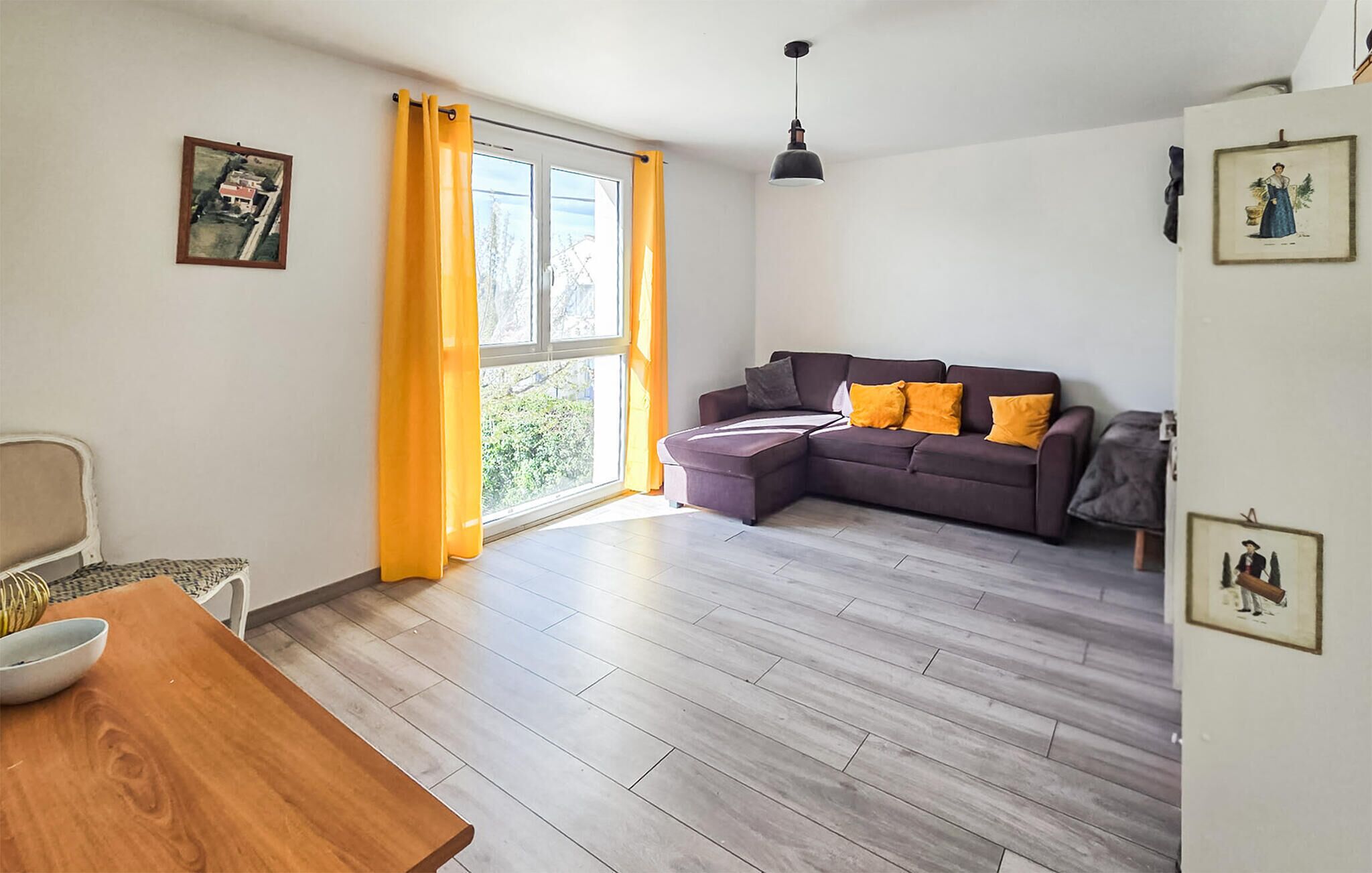A modern living room with a sectional sofa, a dining table, and a large window with curtains.