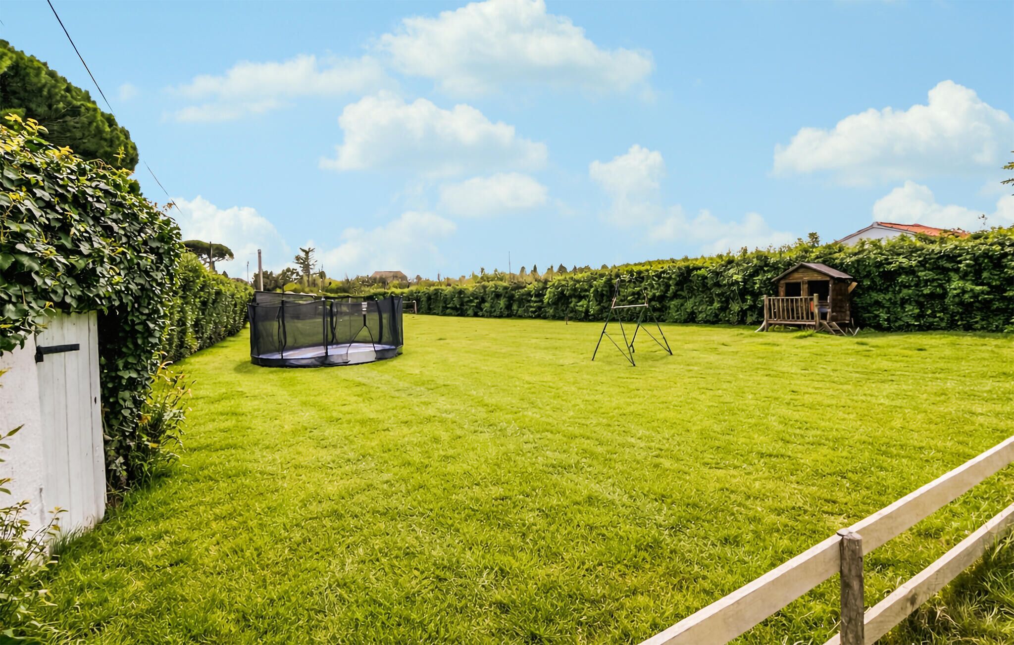 A well-maintained lawn with a trampoline and a wooden playhouse.