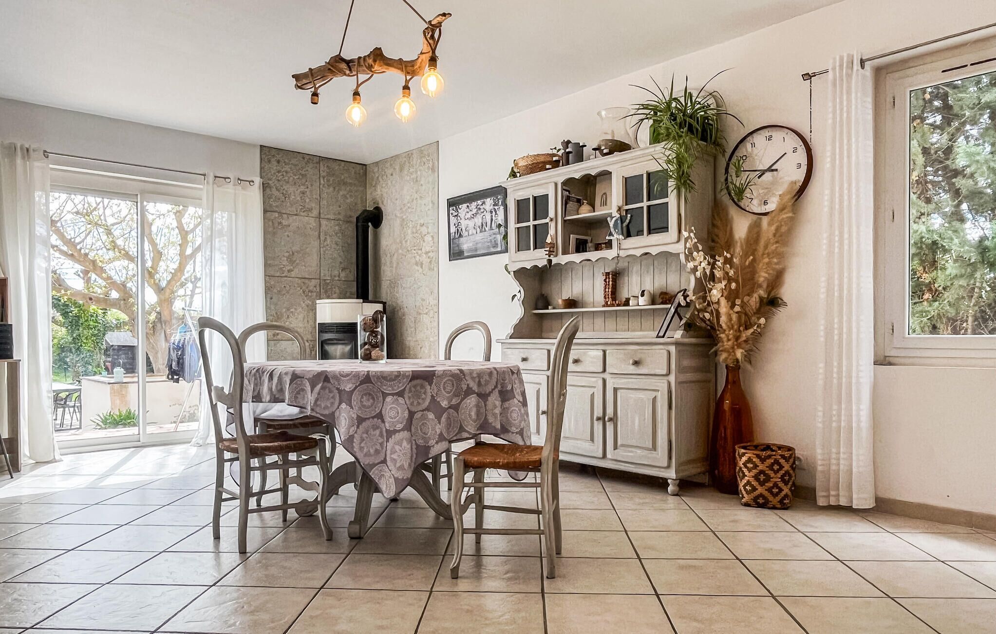Een eetruimte met een tafel, stoelen, een kroonluchter, een klok en uitzicht door een raam.