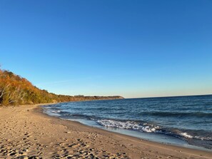 Una playa con cielos despejados, una orilla arenosa y un acantilado con vegetación al fondo.