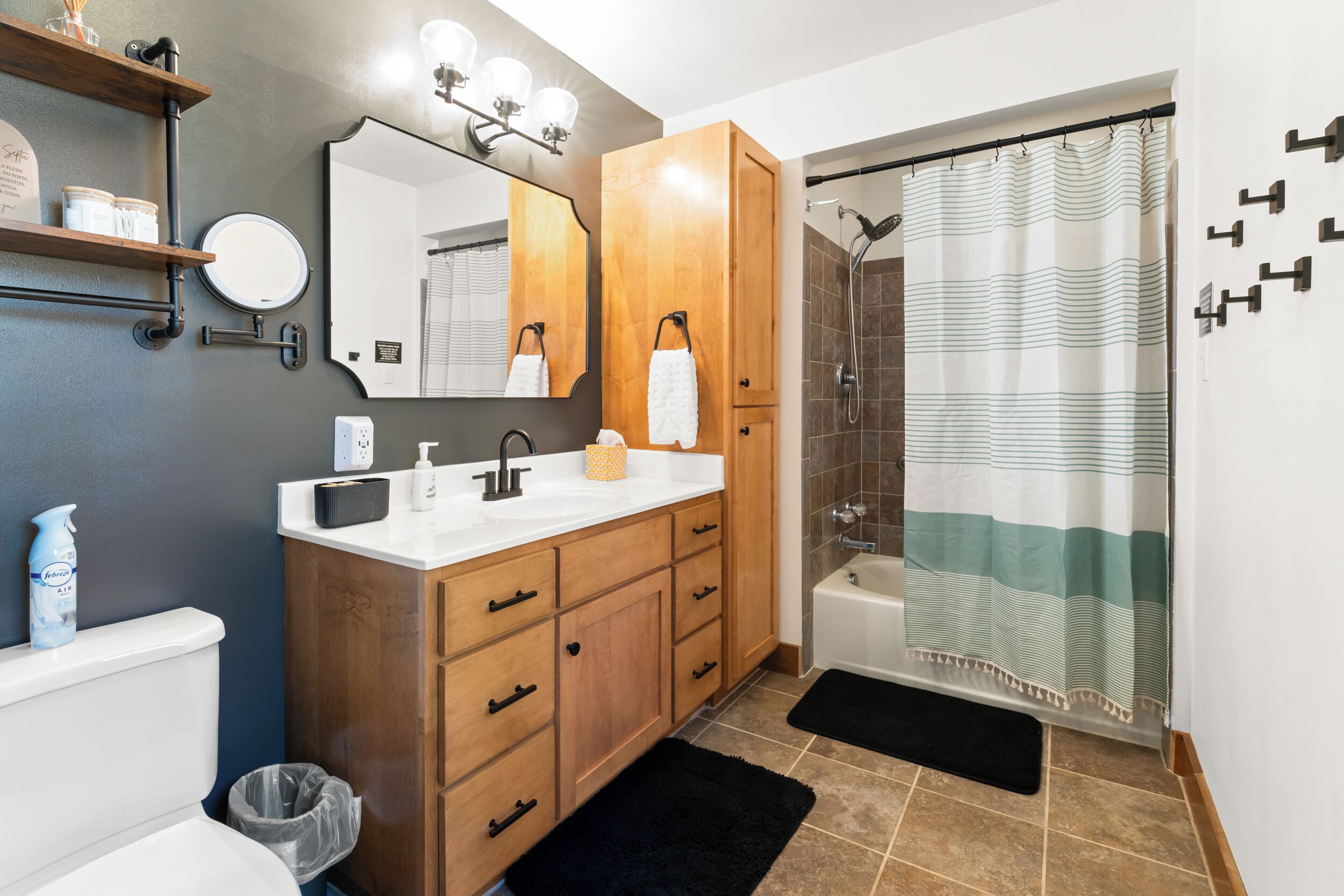 A bathroom with a wooden vanity, a round mirror, a shower with a striped curtain, and a black mat.