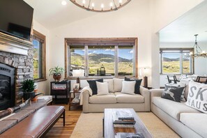A living room with a stone fireplace, a sofa set, a coffee table, and a view of a landscape through large windows. - Perfect Summer Getaway! Recreation Meets Relaxation- Minutes to Lake! (Heber City)