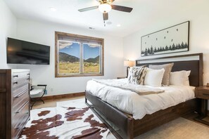 A bedroom with a bed, a ceiling fan, a TV, a window with a mountain view, and a framed picture on the wall. - Perfect Summer Getaway! Recreation Meets Relaxation- Minutes to Lake! (Heber City)