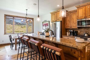 A kitchen with wooden cabinets, a stainless steel refrigerator, a large island with bar stools, and a view of the outdoors through large windows. - Perfect Summer Getaway! Recreation Meets Relaxation- Minutes to Lake! (Heber City)