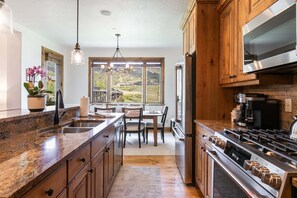 Una cocina con encimeras de granito, armarios de madera, una estufa de acero inoxidable y un amplio ventanal con vistas a un paisaje pintoresco.