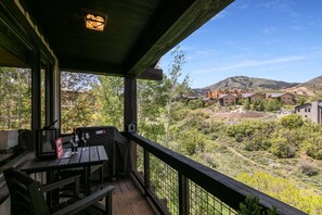 A covered outdoor area with a table and chairs, overlooking a hilly landscape with buildings. - Perfect Summer Getaway! Recreation Meets Relaxation- Minutes to Lake! (Heber City)