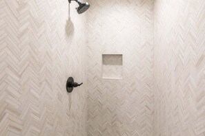 A shower with a herringbone tile pattern, a square recess in the wall, and a showerhead. - Perfect Summer Getaway! Recreation Meets Relaxation- Minutes to Lake! (Heber City)