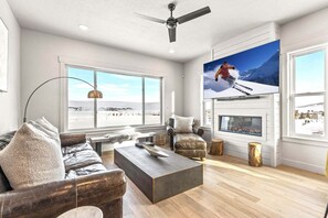 A spacious living room with a fireplace, large windows, a sofa, and a coffee table. - Mountain Escape | Golf Simulator, E-Bikes & Game Room Fun PET FRIENDLY (Park City)