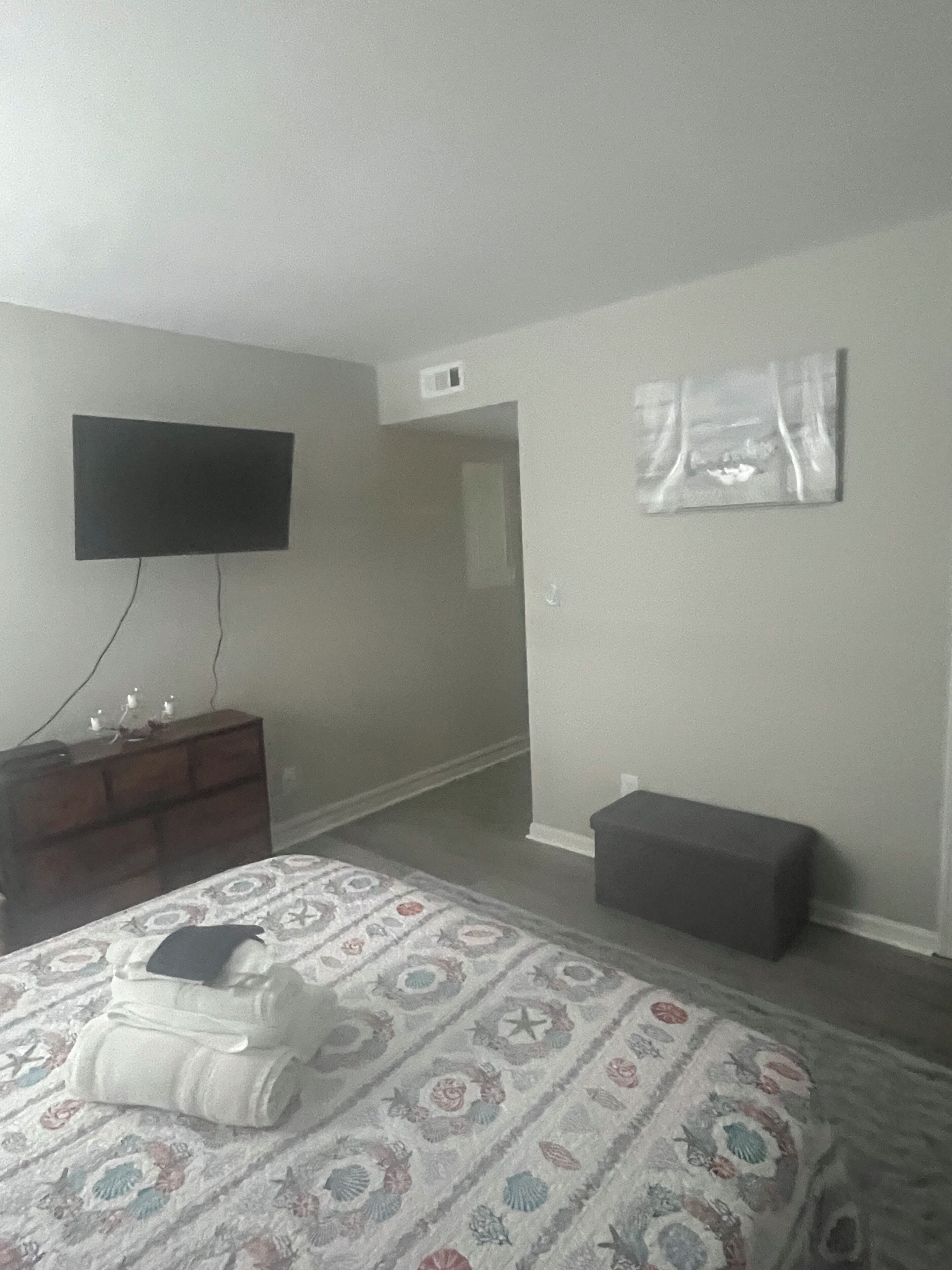 A bedroom with a bed, a dresser, a television mounted on the wall, and a small bench.