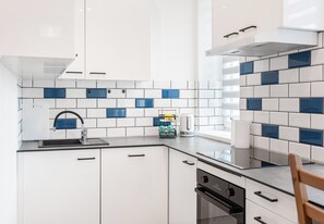 Une cuisine moderne avec des meubles blancs, un plan de travail noir et des carreaux bleus et blancs.