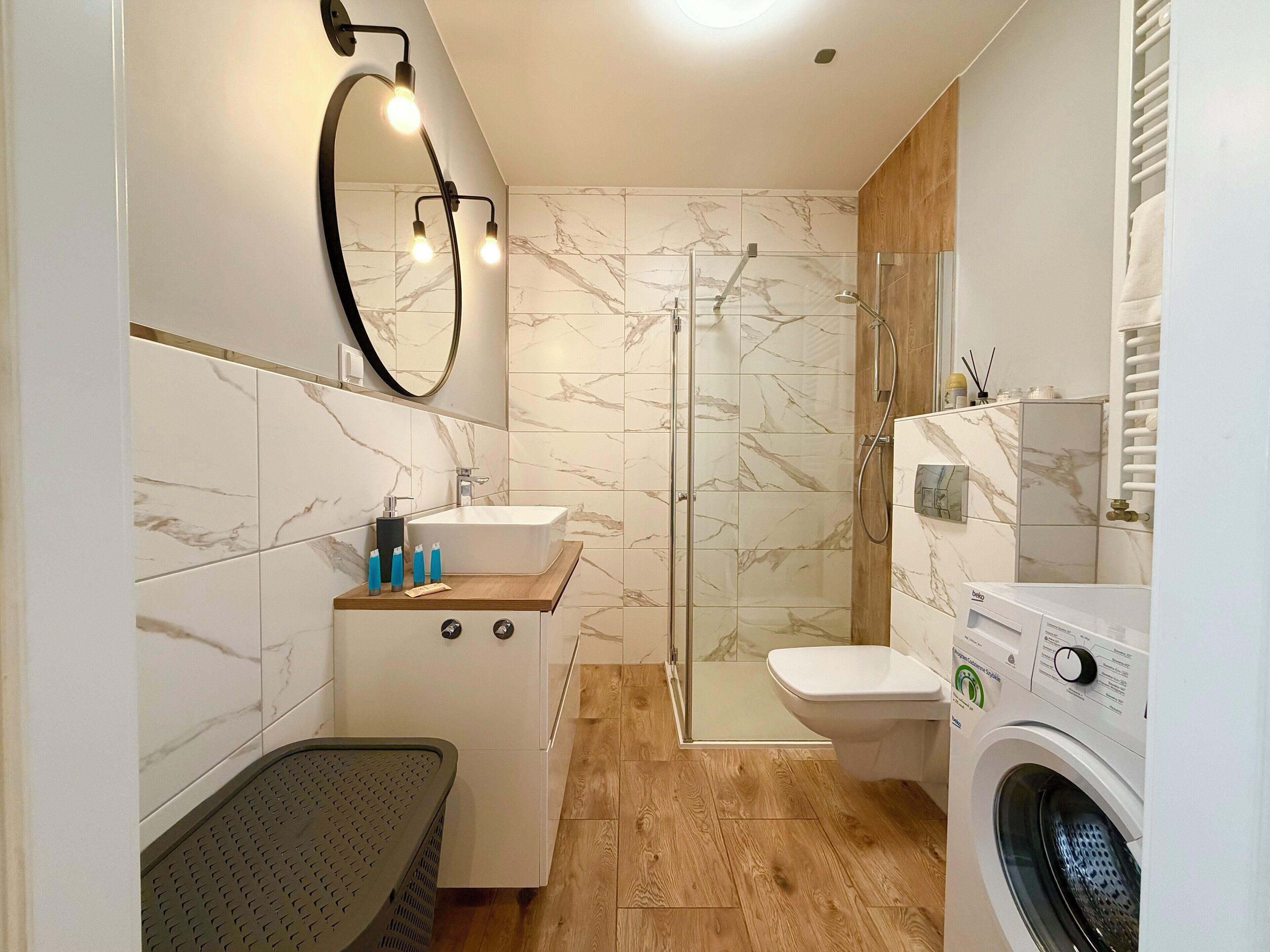 A modern bathroom with a shower, toilet, sink, and washing machine.