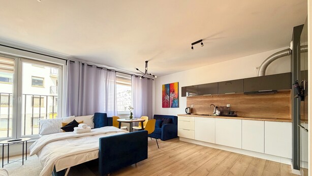 Et moderne hotelværelse med seng, lille bord, sofa, tekøkken og udsigt over byen.