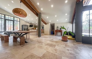 A spacious living area with a large wooden table, a hanging light fixture, and a potted plant.