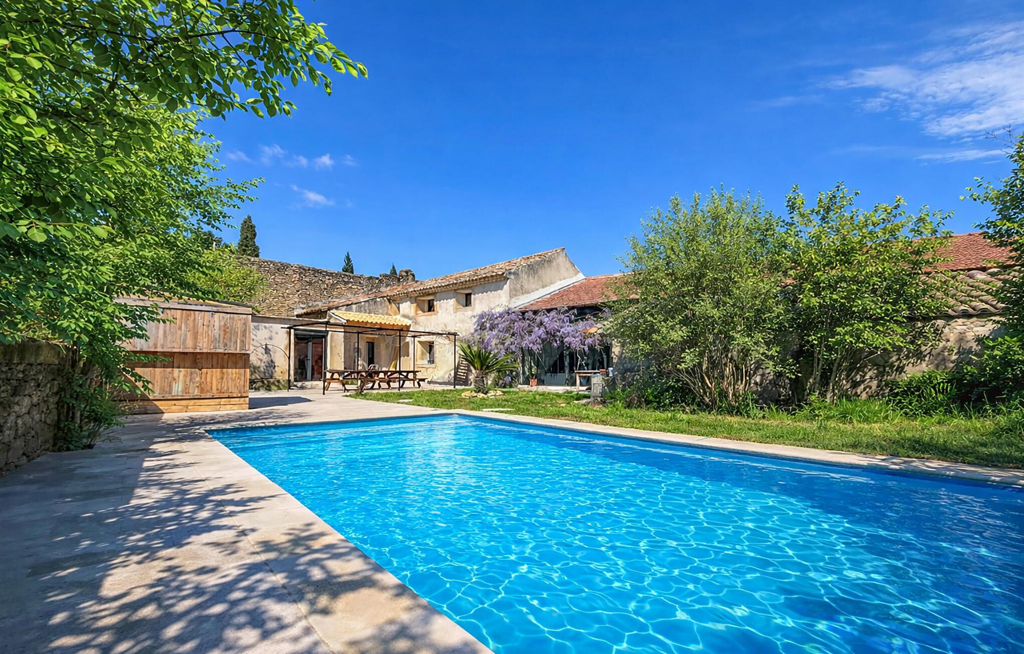 Une piscine avec un espace patio, un mur en pierre et un bâtiment doté d’un toit en tuiles.