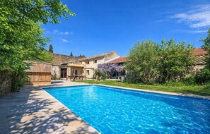 A swimming pool with a patio area, a stone wall, and a building with a tiled roof.